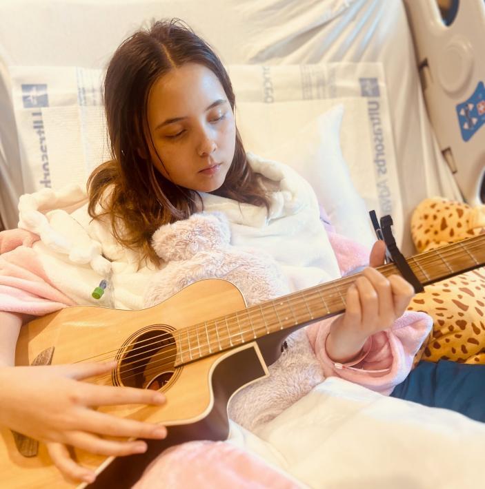 Phoenix is playing guitar while sitting up in her hospital bed