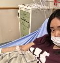 Young woman, wearing a hospital mask, is in a hospital bed, with her vein hooked up to equipment