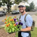Allen is standing outside with a large tray of Pansy flowers. He wears a cap and has a large smile on his face.